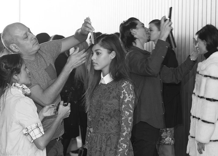 PANYC stylists comb and style models' hair together in the busy backstage area, shot in black and white.
