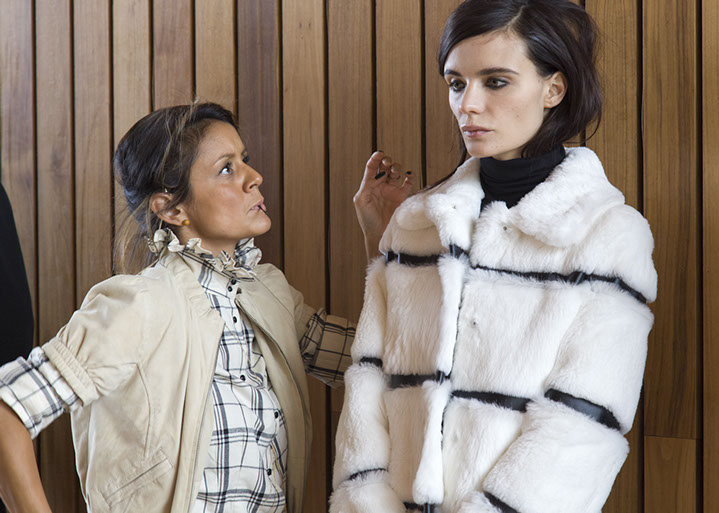 A PANYC stylist adjusts the hair of a model wearing a black-and-white striped fur coat backstage before the Blue Les Copains presentation.