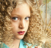 Close-up of a model's tight blonde ringlet curls and red lipstick, holding a paper fan